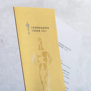 Glossy Spot UV Varnish applied to gold "Spordiaasta Tähed" gala invitations, creating a shimmering reflective athlete silhouette on a matte gold cardstock.