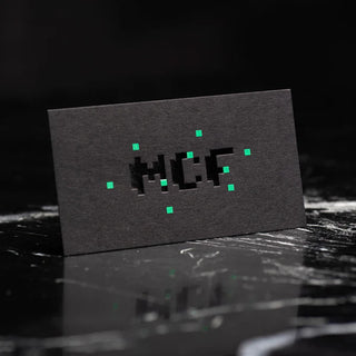Premium black foil business cards with a textured matte finish and neon green pixel accents on a dark marble surface.