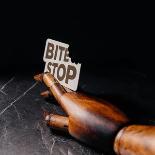 White business card die-cut with a bite mark shape reading "BITE STOP" in brown text, propped against the fingers of a wooden artist's mannequin hand on a dark marble surface.
