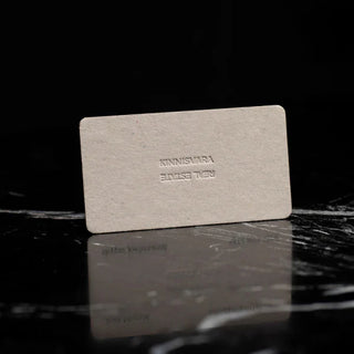 Minimalist embossed business cards for a real estate company featuring a blind emboss on grey recycled cardstock.