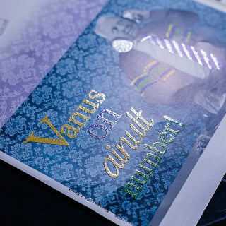 Close-up of yellow and green glitter screen printing on a blue damask patterned card.