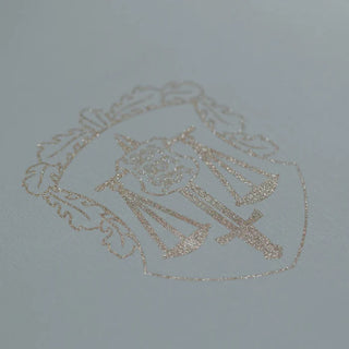 Custom glitter screen printing of a gold metallic coat of arms featuring the scales of justice and a sword on white cardstock.