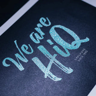 Vibrant glitter screen printing on neon blue lettering over a dark textured background.