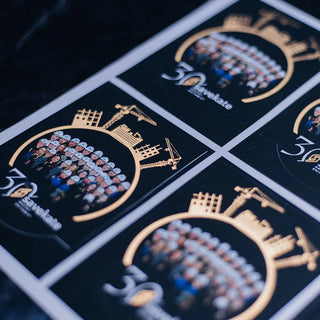 Custom gold screen printing stickers for Savekate's 30th anniversary featuring metallic gold construction crane illustrations and a team photo.