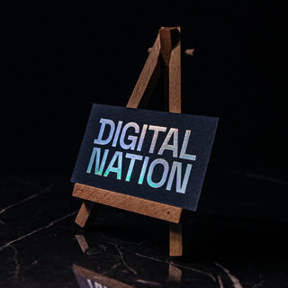 Premium holographic foil business cards showing a rainbow shimmer effect on the company logo against a dark marble surface.