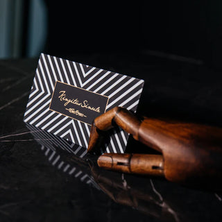 Metallic screen printing in gold script on a black and white striped gift card, displayed with a wooden artist hand.