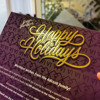 Custom raised foil printing on a purple holiday card featuring a textured gold "Happy Holidays" script.