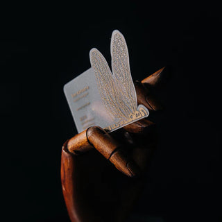 Translucent business card with gold screen printing on plastic, held by a wooden hand to show transparency.